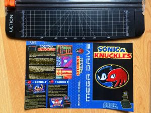 Bereits ausgeschnittenes Sonic-&-Knuckles Custom Cover für das Sega Mega Drive neben einem Schneidegerät